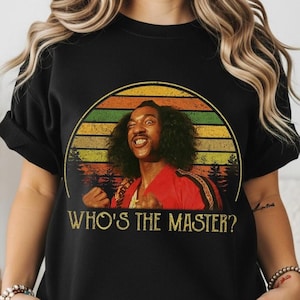 May include: Black t-shirt featuring a retro-style graphic of a man in a red jacket with the text "WHO'S THE MASTER?" in gold lettering. The graphic is set against a sunset-colored background.