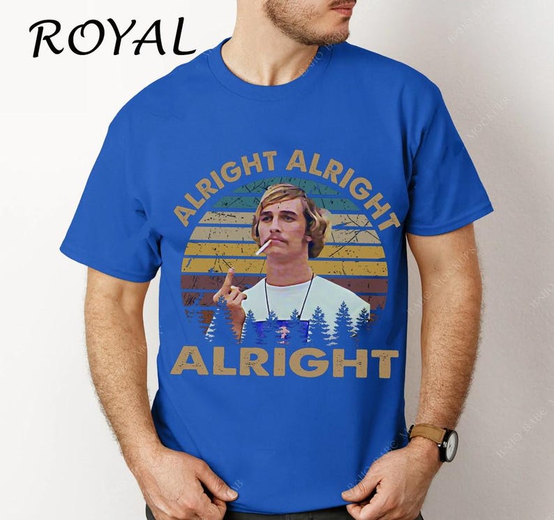 Puede incluir: Camiseta azul real con un gr&aacute;fico de un hombre y el texto "ALRIGHT ALRIGHT ALRIGHT" en un dise&ntilde;o circular. El dise&ntilde;o incluye una puesta de sol y &aacute;rboles. La palabra "ROYAL" est&aacute; impresa en la parte superior izquierda.