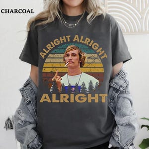 Puede incluir: Camiseta de color carb&oacute;n con la frase "ALRIGHT ALRIGHT ALRIGHT" y una imagen de un hombre con un cigarrillo. El dise&ntilde;o incluye un fondo estilo puesta de sol e im&aacute;genes de bosque.