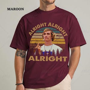 Puede incluir: Camiseta granate con un dise&ntilde;o retro. El dise&ntilde;o presenta el texto "ALRIGHT ALRIGHT ALRIGHT" alrededor de una imagen de un hombre con un cigarrillo, sobre un fondo de puesta de sol y silueta de bosque. La palabra "MAROON" est&aacute; impresa en la parte superior izquierda.
