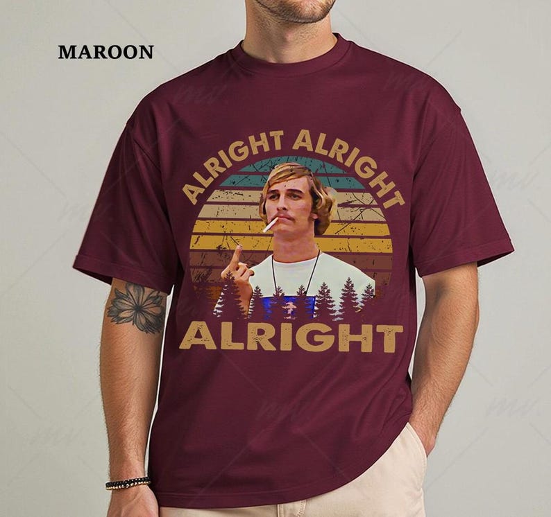 Puede incluir: Camiseta granate con un dise&ntilde;o retro. El dise&ntilde;o presenta el texto "ALRIGHT ALRIGHT ALRIGHT" alrededor de una imagen de un hombre con un cigarrillo, sobre un fondo de puesta de sol y silueta de bosque. La palabra "MAROON" est&aacute; impresa en la parte superior izquierda.