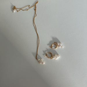 May include: A gold chain necklace and a pair of gold hoop earrings, both with white pearl accents.