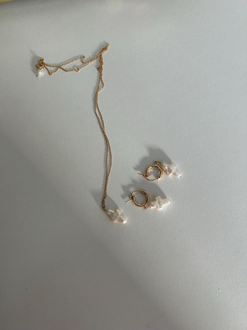 May include: A gold chain necklace and a pair of gold hoop earrings, both with white pearl accents.