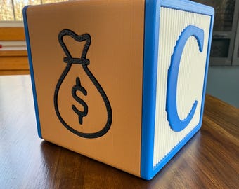 May include: A brown wooden block with a blue border and a white face. The white face has a blue letter "C" on it. The brown face has a black outline of a money bag with a dollar sign inside.