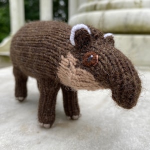 Könnte beinhalten: Ein braunes, gestricktes Stofftier, das einem Tapir ähnelt, mit einer langen Schnauze, braunem Fell und weißen Markierungen um die Augen.
