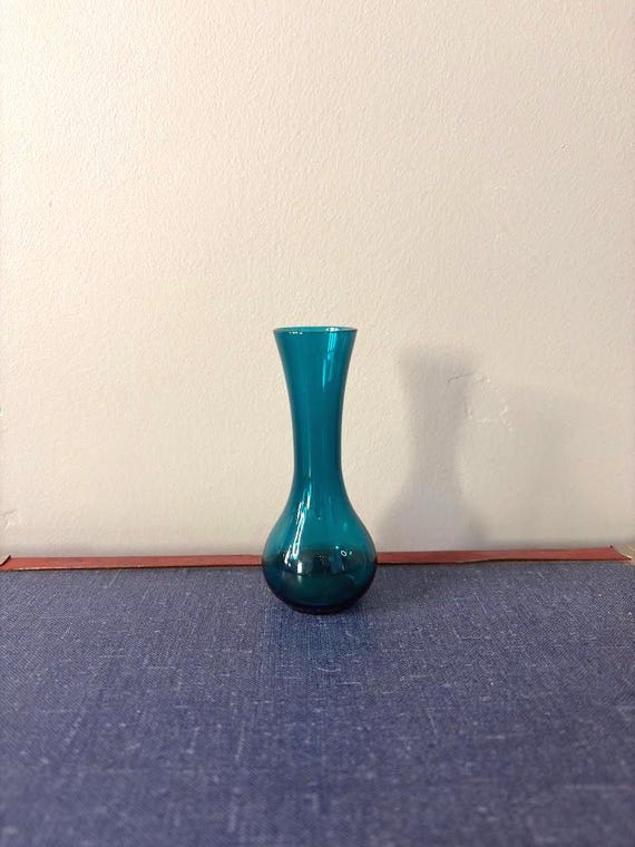 Tiny mouth-blown turquoise glass bud vase with a vintage sensibility — the kind of object that looks like it belongs in an antique shop, not a Fulfillment Center.