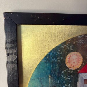 The top left corner of the black wooden frame showing signs of surface scratches and aged texture. This corner includes a visible portion of the red sun, teapot lid, and deep blue background pattern that resembles embroidered fabric.