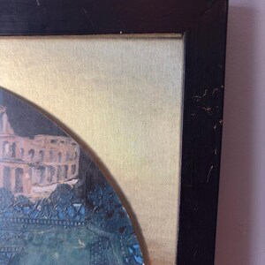Corner view of the top right section of the black wooden frame, showing slight scuffing and wear on the edges. The metallic gold backing of the artwork contrasts with the vibrant blue collage inside the circular artwork window.