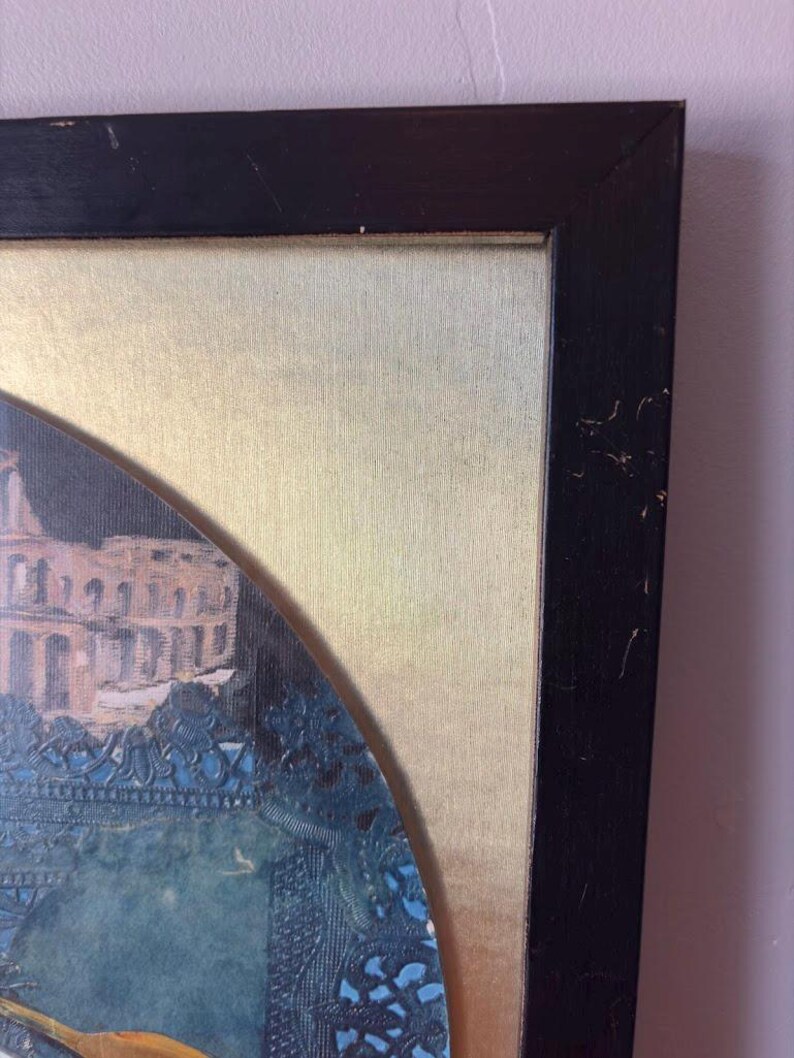 Corner view of the top right section of the black wooden frame, showing slight scuffing and wear on the edges. The metallic gold backing of the artwork contrasts with the vibrant blue collage inside the circular artwork window.
