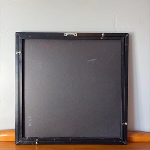 Rear view of the framed artwork showing a matte black back panel with wall mounting hardware. The number "9504" is printed in the lower-left corner, and the frame has metal corner brackets for secure hanging.