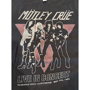 以下が含まれることがあります： Mötley Crüeのバンドロゴとメンバー4人が描かれた白いグラフィックがプリントされた黒いTシャツ。背景には大きなピンクの三角形が配置されている。テキストにはMötley Crüe、Live in Concert、Glendale Civic Auditorium - May 7th, 1982と記されている。