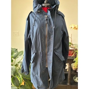 Può includere: Giacca con cappuccio blu navy con vita regolabile con coulisse e chiusura a zip. La giacca ha più tasche e dettagli con bottoni. La giacca è esposta su un manichino. La giacca è di media lunghezza.