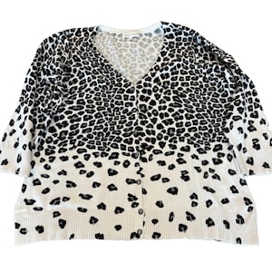 May include: A V-neck cardigan with a button-down front and three-quarter sleeves. The sweater displays a black and white leopard print. The pattern fades towards the bottom of the garment.