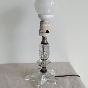 May include: A clear glass table lamp with a star-shaped base and a white glass globe shade. The lamp has a silver-coloured metal base and a textured glass stem.