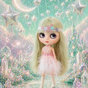 Pode incluir: Uma boneca com cabelo comprido verde claro e um vestido rosa com saia de penas. A boneca usa uma faixa com detalhes de estrelas. O fundo apresenta uma cena brilhante e sonhadora com estrelas, uma lua crescente e um castelo.