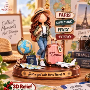 May include: A decorative figurine featuring a girl with long brown hair wearing a hat, green jacket, and jeans, standing next to a pink suitcase labeled Emma and 2026. The base includes a globe, a passport, a small airplane, and a signpost for Paris, New York, Italy, and Tokyo, with the text Just a girl who loves Travel on the front.