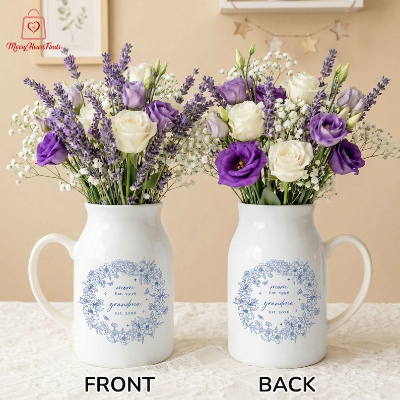 Puede incluir: Dos jarrones de cer&aacute;mica blanca con asas, cada uno con un ramo de lavanda morada, rosas blancas y paniculata. Los jarrones tienen un dise&ntilde;o floral azul con las palabras "mam&aacute;" y "abuela" y los a&ntilde;os "Est. 1996" y "Est. 2020".