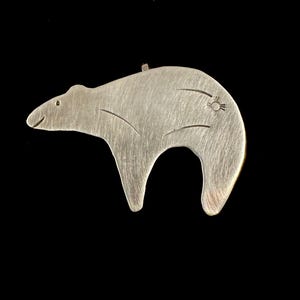 Op de afbeelding: Een zilverkleurige berenhanger met geëtste details. De beer heeft een klein zonontwerp op zijn rug en een kleine lus aan de bovenkant om op te hangen. De hanger staat tegen een zwarte achtergrond.