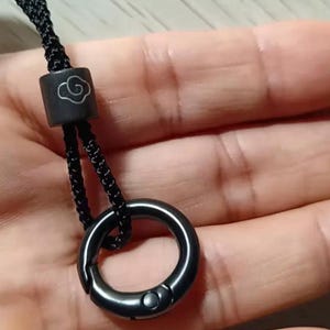 May include: Black lanyard with a metal ring and a cylindrical bead featuring a cloud design. The lanyard is made of a braided black cord. The metal ring has a spring-loaded clasp.