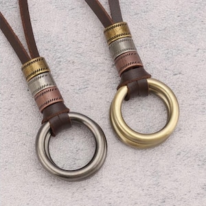 May include: Two pendant necklaces with large metal rings. One ring is silver, the other is gold. The necklaces have brown leather cords and decorative metal bands in gold, silver, and copper tones.
