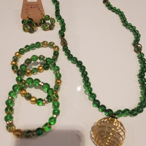 May include: A green glass bead necklace with a gold pendant, a matching bracelet, and a pair of earrings. The necklace and bracelet have gold accents.