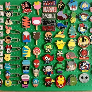May include: A collection of colorful enamel pins featuring various Disney and Marvel characters, ice cream treats, and license plate designs. The pins are attached to a green pin board with safety pins.