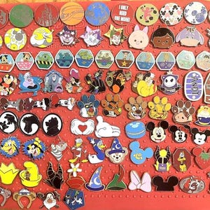 May include: A collection of Disney character pins, including Mickey Mouse, Donald Duck, and other popular characters. The pins are in various shapes and colors, arranged on a red surface. Some pins feature text like "I only need one more!"