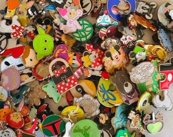 May include: A large collection of assorted metal enamel pins featuring various cartoon characters, including Mickey Mouse, Minnie Mouse, Yoda, and Daisy Duck, alongside colorful shapes like a polka-dot bag, a macaron, and a teacup.