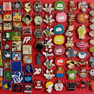 May include: A collection of colorful Disney character pins and watches arranged on a red surface. The pins feature various characters like Mickey Mouse, Winnie the Pooh, and others. Some pins have text, including "Pooh" and "I ONLY NEED ONE MORE!"