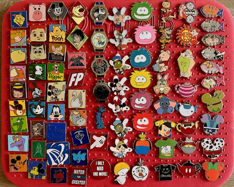 May include: A collection of colorful Disney character pins and watches arranged on a red surface. The pins feature various characters like Mickey Mouse, Winnie the Pooh, and others. Some pins have text, including "Pooh" and "I ONLY NEED ONE MORE!"