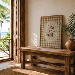 Op de afbeelding: Een rechthoekig ingelijst kunstwerk met een beige en witte gingham-achtergrond. In het midden bevindt zich een ovaal stoffen inzetstuk met een botanische illustratie van rode aardbeien en groene bladeren, omrand door een cr&egrave;mekleurige gehaakte kanten rand.