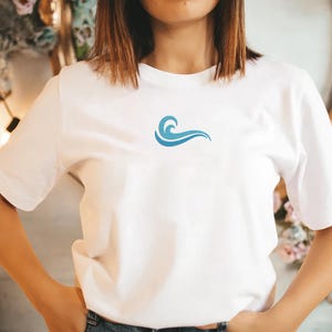 May include: White t-shirt with a small, blue wave design on the chest. The short-sleeved shirt is made of a soft material and is suitable for casual wear. The wave graphic is a simple, stylized design.