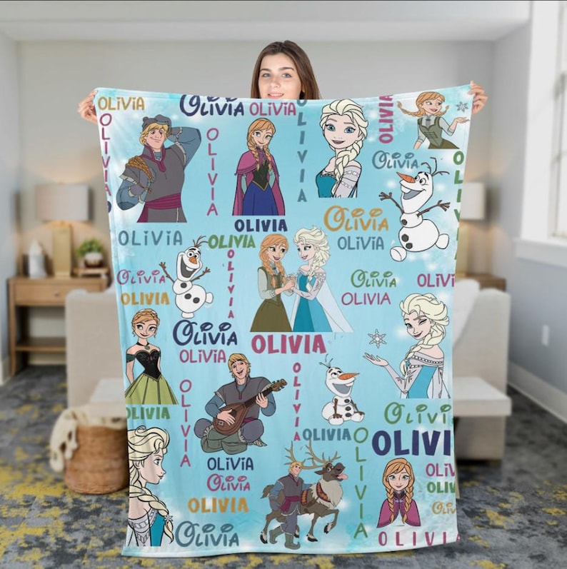 May include: A light blue blanket featuring characters from the movie Frozen, with the name "Olivia" repeated throughout. The blanket showcases illustrations of Elsa, Anna, Olaf, Kristoff, and other characters.