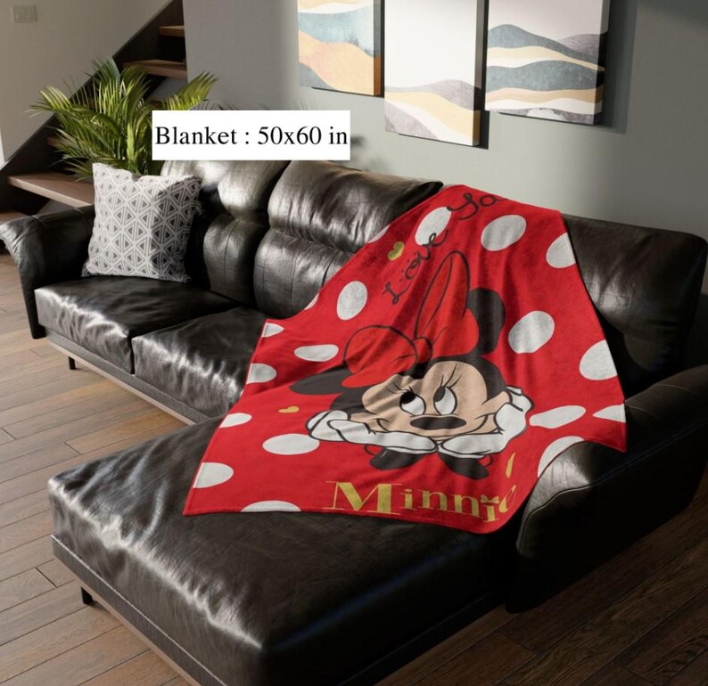 May include: A red blanket with white polka dots and a Minnie Mouse graphic. The blanket measures 50 x 60 inches and features the word "Minnie" in gold lettering. The blanket is draped over a black leather couch.