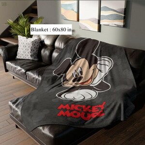 May include: A black blanket featuring a large Mickey Mouse graphic and the words "Mickey Mouse" in red. The blanket measures 152x203 cm and is draped over a black leather sofa.
