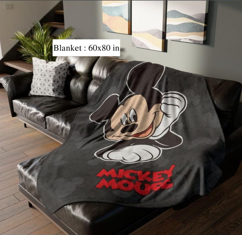 May include: A black blanket featuring a large Mickey Mouse graphic and the words "Mickey Mouse" in red. The blanket measures 152x203 cm and is draped over a black leather sofa.