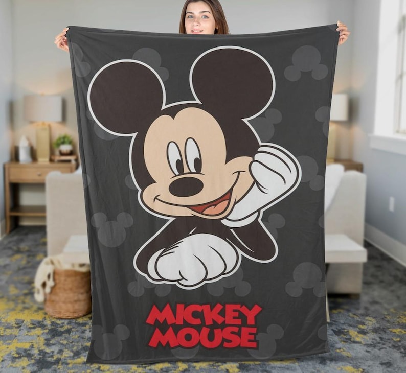 May include: A dark grey blanket with a large illustration of Mickey Mouse. The cartoon character is smiling with his right hand raised. The words "Mickey Mouse" are printed in red at the bottom of the blanket. Mickey Mouse silhouettes are in the background.
