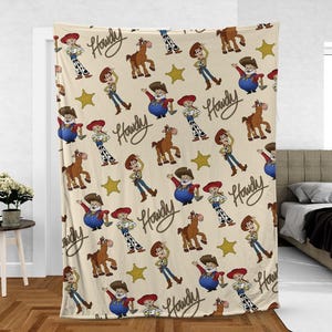 May include: A beige blanket with a repeating pattern of cartoon characters, a horse, and gold stars. The word "Howdy" is written in a brown script across the blanket. The blanket is draped over a doorway.