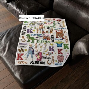May include: A white blanket, 30 x 40 inches, featuring colorful cartoon characters and the name "Kieran" in various fonts. The blanket has a repeating pattern of stars, horseshoes, and the letter "K".