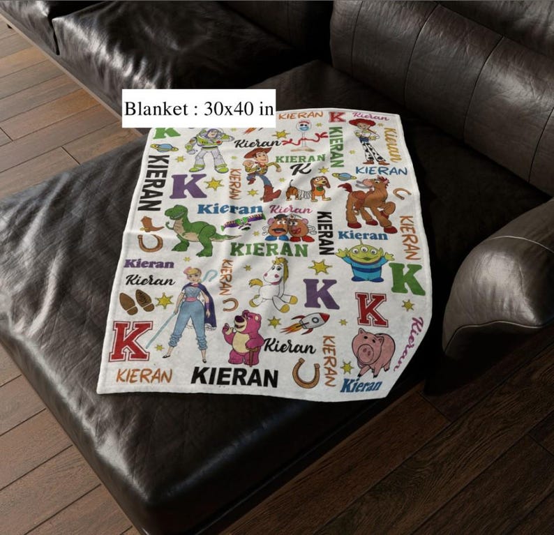 May include: A white blanket, 30 x 40 inches, featuring colorful cartoon characters and the name "Kieran" in various fonts. The blanket has a repeating pattern of stars, horseshoes, and the letter "K".