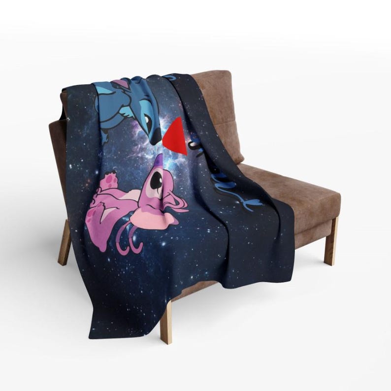 May include: A navy blue throw blanket featuring a space-themed design with cartoon characters. The blanket showcases a blue alien and a pink alien with a red heart between them. The blanket is draped over a brown chair.