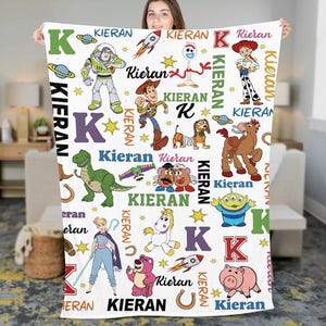 May include: A white blanket featuring various Toy Story characters, the letter "K", and the name "Kieran" in multiple fonts and colors. The blanket includes images of Buzz Lightyear, Woody, and other characters from the animated film.