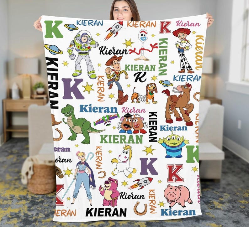 May include: A white blanket featuring various Toy Story characters, the letter "K", and the name "Kieran" in multiple fonts and colors. The blanket includes images of Buzz Lightyear, Woody, and other characters from the animated film.