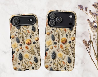 May include: Two phone cases featuring a repeating pattern of dried botanical elements including dark blue thistle, orange protea, yellow flowers, and various ferns on a cream background. The cases have black camera cutouts.