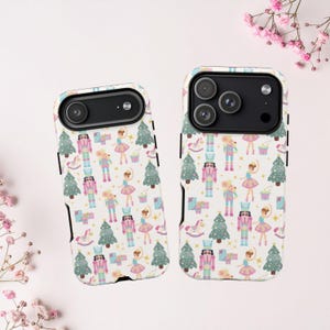 Puede incluir: Dos fundas para teléfono con un patrón repetido de ilustraciones navideñas. El diseño incluye cascanueces, bailarinas, ratones, árboles de Navidad y caballos balancín en colores pastel sobre un fondo blanco. Las fundas tienen bordes negros.
