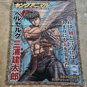 Könnte beinhalten: Gewebte Überwurfdecke mit einer Manga-Illustration. Das Design zeigt einen muskulösen Charakter mit einem großen Schwert, japanischem Text und einem Farbschema aus Blau, Braun und Beige. Die Decke hat einen Fransenrand.