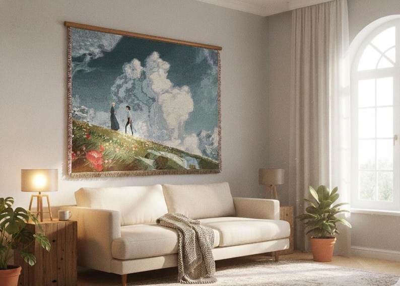 May include: A tapestry wall hanging with a landscape scene featuring two figures on a hillside with clouds. The tapestry is framed with a wooden rod and is displayed above a cream-colored sofa. The room has a neutral color palette.