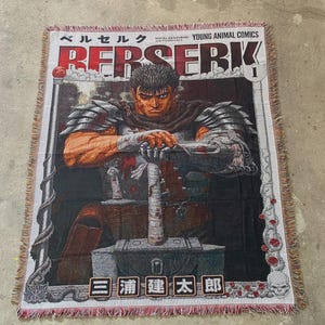 May include: Woven throw blanket with a manga illustration of a warrior with a sword. The blanket features the title "BERSERK" in bold letters and Japanese text. It has a fringed edge and a detailed, colourful design.