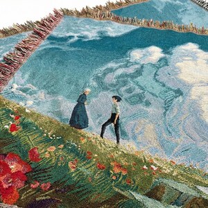 May include: Woven throw blanket featuring a landscape scene with figures on a hillside with red flowers. The background depicts a cloudy sky and a body of water. The blanket has a fringed edge.