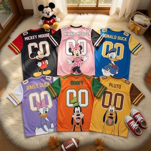 Puede incluir: Surtido de camisetas de personajes de Disney, incluyendo Mickey Mouse, Minnie Mouse, Donald Duck, Daisy Duck, Goofy y Pluto. Cada camiseta presenta un gráfico del personaje y el número "00". Las camisetas son de varios colores, con zapatillas a juego y un balón de fútbol americano.